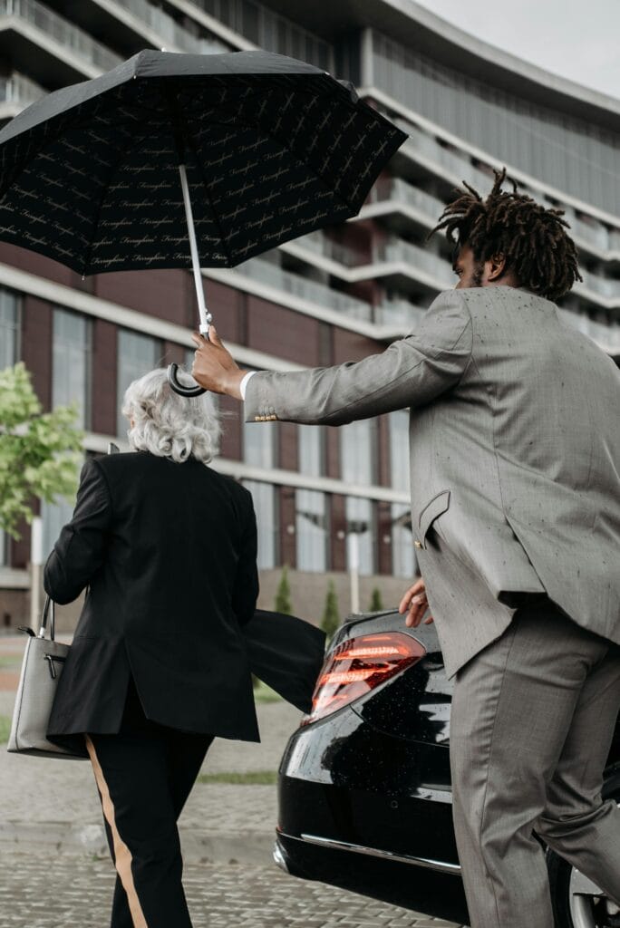 pexels-photo-8425352-8425352 Two business professionals with an umbrella near a luxury car in an urban setting.